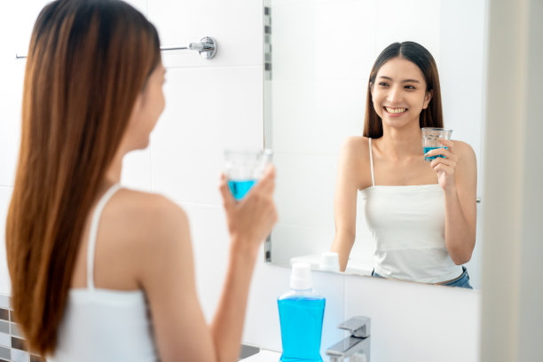 年轻的亚洲女子在洗手间用漱口水清洁牙齿。用漱口水清洁口腔，保持口腔健康。图片下载