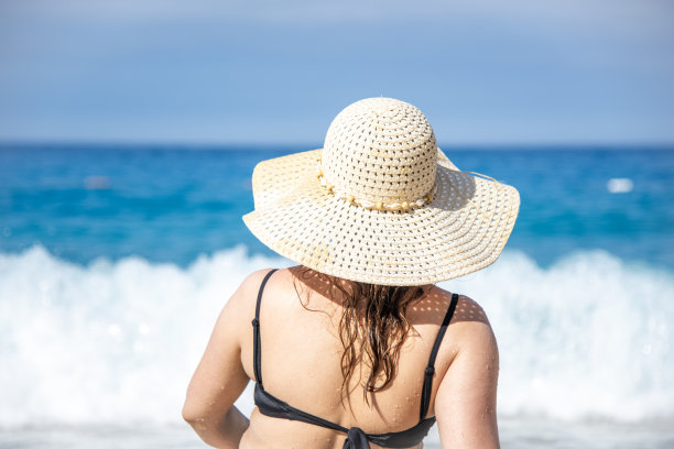 戴着白帽子躺在沙滩上的女人。戴着太阳草帽晒日光浴。夏季沙滩度假和度假旅游的概念。大海和蓝天的背景。图片下载