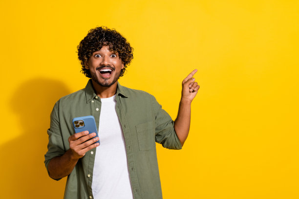 年轻有趣的卷发墨西哥人用他的智能手机的照片震惊浏览新闻直接手指网站孤立的黄色背景图片下载