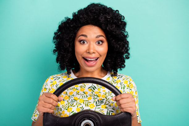 照片的迷人的积极的女人穿花t恤骑汽车空旷的空间孤立的绿松石色背景图片下载