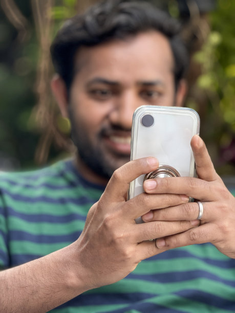特写图片:印度男子穿着休闲服装蓝绿条纹t恤，在公园区域靠在椅子上，手持手机看智能手机屏幕，肖像，焦点在前景图片下载