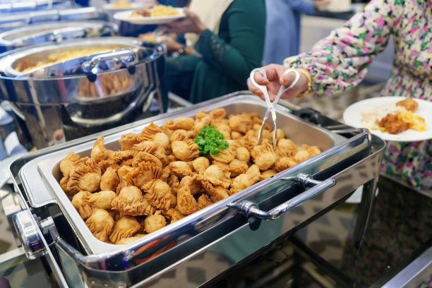 这张经过剪裁的照片捕捉了排队的商人们，他们用上菜勺从自助餐中挑选食物。图片下载