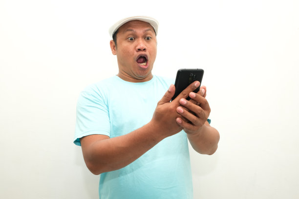 照片中，一名亚洲男子看着手中的手机，露出震惊的表情图片下载