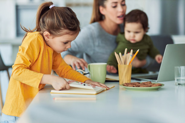 一个可爱的小女孩在她妈妈照顾她的孩子时从笔记本上撕下她的画图片下载