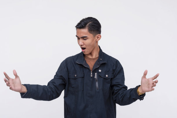 一个惊讶的菲律宾年轻人急切地描述着什么大东西。穿着一件黑色夹克。孤立在白色背景上。图片下载