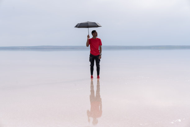 身着黑色西装、打着红色雨伞的商人站在盐湖上图片下载