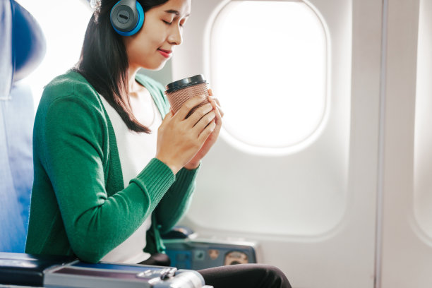 一个年轻的亚洲女人，一个飞机乘客，通过她的手机听音乐放松。她在长途旅行中使用科技来放松。图片下载