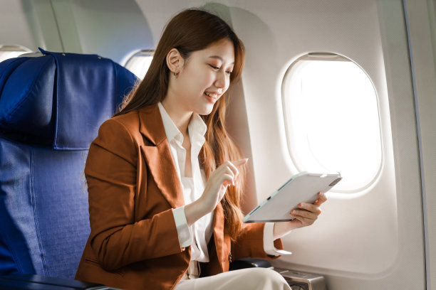 一位年轻的亚洲女商人穿着正装，坐在飞机座位上，拿着笔记本电脑和公文包，利用飞机上的Wi-Fi进行电话会议。图片下载