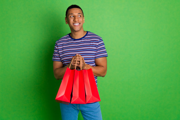 照片中，高兴的好男人穿着条纹时髦的衣服，拿着包裹，在绿色的背景上看起来空无一物图片下载