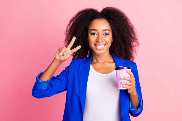 可爱的漂亮女孩穿着时尚的蓝色衣服，在粉红色的背景上享受咖啡v字图片下载