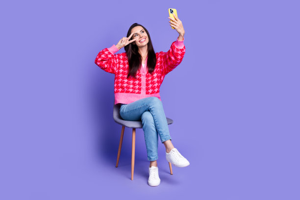 闪亮迷人的女士穿着粉红色开襟羊毛衫的全身照片，显示v字标志，自拍现代设备孤立的紫罗兰色背景图片下载
