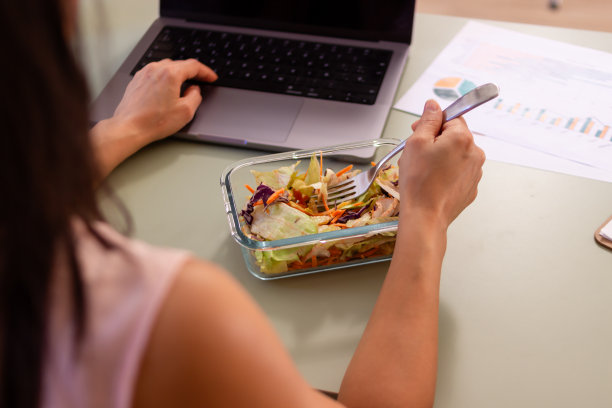 女商人在办公室吃沙拉，用笔记本电脑工作图片下载