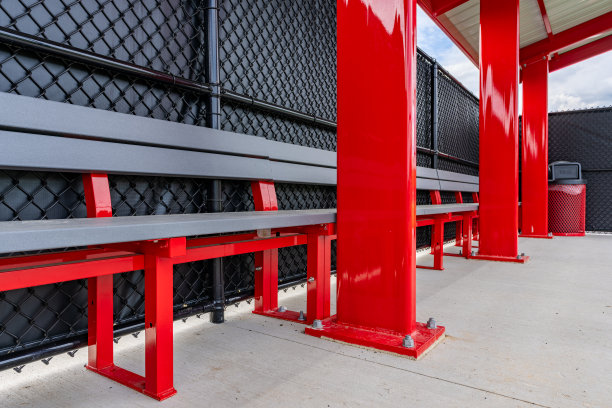 一个红色垒球棒球教练席的内部照片，有屋顶、混凝土地板和红色和灰色的球队板凳。图片下载