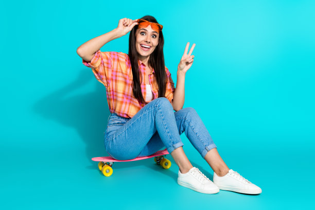 可爱的年轻女士的全尺寸照片坐滑板太阳镜v标志穿着时尚的格纹服装孤立的海蓝宝石色背景图片下载