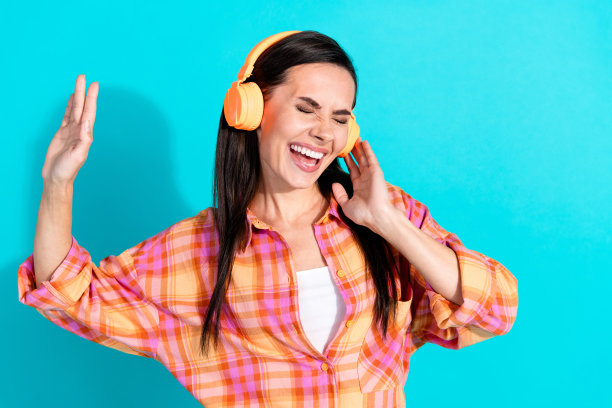 迷人的年轻女子的照片肖像，耳机，听音乐，唱歌穿着时尚的格纹衣服孤立的海蓝宝石色背景图片下载