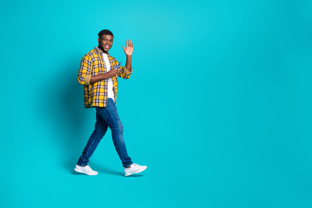 照片正面有魅力的男人穿着时髦的衣服，拿着现代设备，在青色的背景上走空旷的空间图片下载