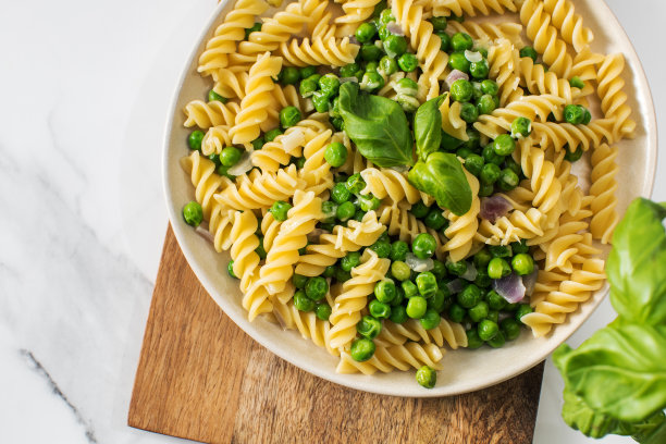 白色大理石餐桌上美味的意大利面配青豆和罗勒图片下载