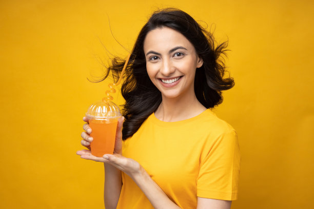 开朗的女孩穿着t恤喝橙汁的肖像孤立在黄色背景股票照片图片下载