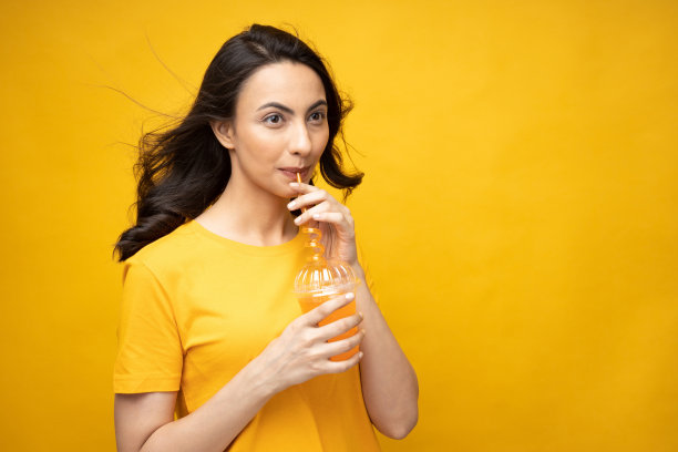 开朗的女孩穿着t恤喝橙汁的肖像孤立在黄色背景股票照片图片下载