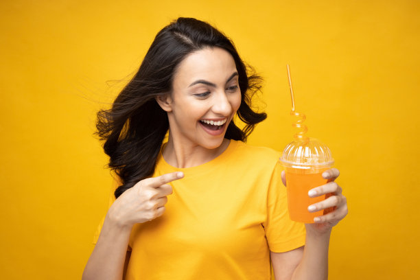 开朗的女孩穿着t恤喝橙汁的肖像孤立在黄色背景股票照片图片下载