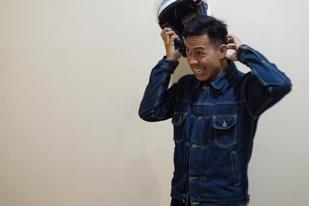 一名东南亚男子身穿牛仔夹克，头上戴着白色摩托车头盔图片下载