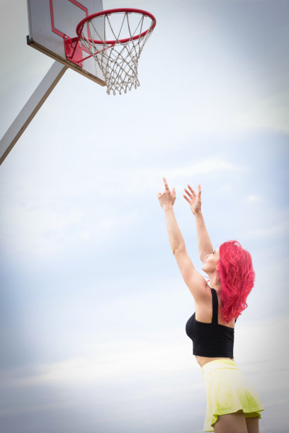 一个穿着鲜艳裙子的漂亮女孩伸手去拿篮球框。图片下载
