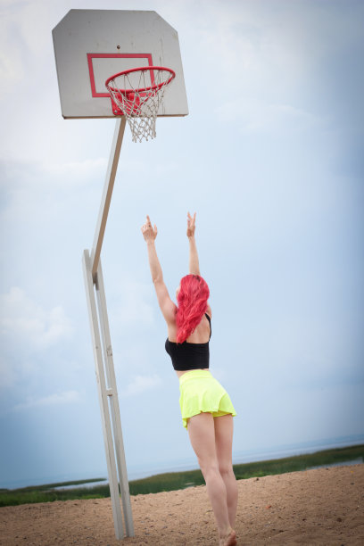 一个穿着鲜艳裙子的漂亮女孩伸手去拿篮球框。图片下载