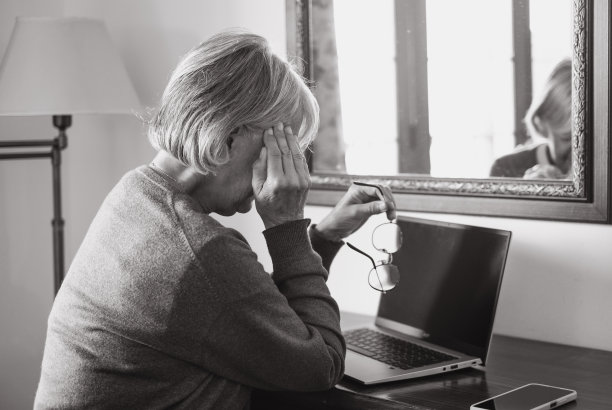 黑白照片，老妇人在家里使用笔记本电脑，同时摸着太阳穴治疗头痛。过度的工作或学习会导致严重的偏头痛图片下载