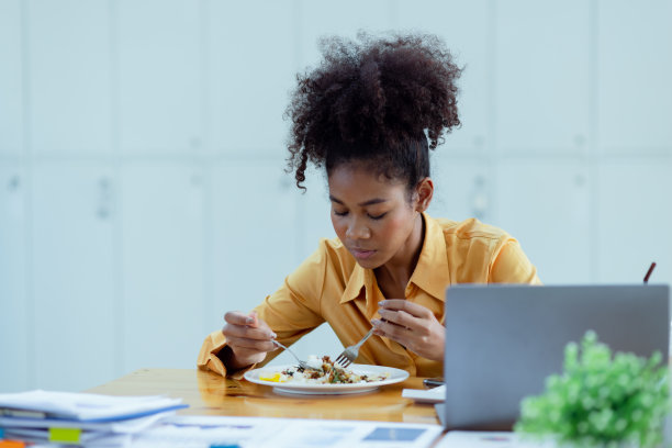 年轻的非裔美国女性在办公桌上吃快餐。图片下载