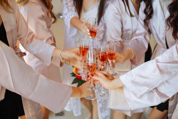 年轻的伴娘在酒店房间里碰杯喝香槟。欢快的女孩庆祝单身派对的特写照片。女性吃吐司配酒图片下载