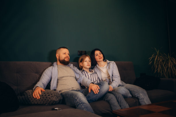 家庭、休闲和人的概念——快乐微笑的爸爸拿着遥控器，妈妈和小女儿晚上在家看电视图片下载