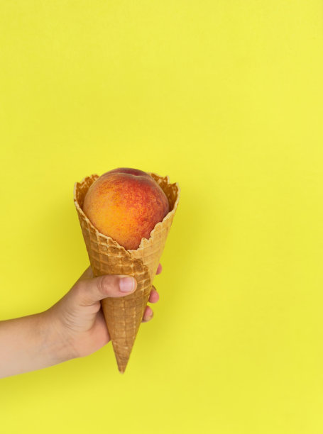 手里拿着桃子味的甜筒冰激凌。黄色背景。最小的夏季概念。本空间图片下载