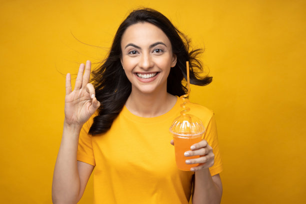 开朗的女孩穿着t恤喝橙汁的肖像孤立在黄色背景股票照片图片下载