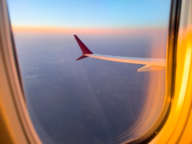 日落时从飞机窗口望向机翼。从飞机窗口鸟瞰云层。飞机的机翼与夕阳的天空图片下载