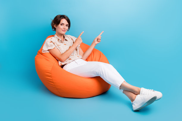 全尺寸照片漂亮的积极的女孩坐在舒适的袋子表明手指空白空间孤立的蓝色背景图片下载