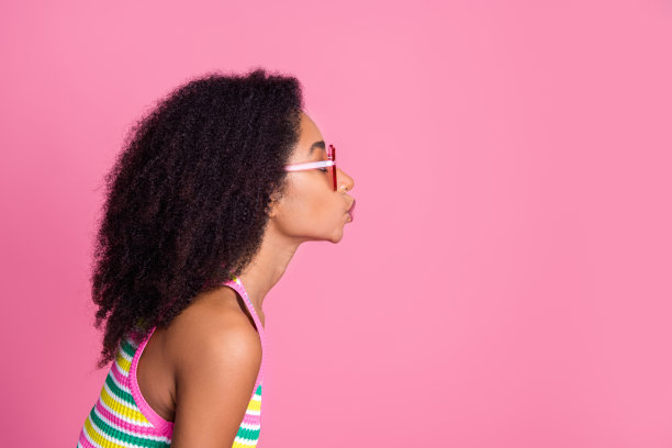 可爱的好心情女孩的侧面照片，戴着彩色的眼镜，在粉红色的背景上给空白的空间送去飞吻图片下载