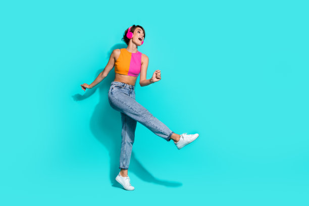 全身照片的酷时髦的女士穿着五颜六色的顶部唱歌，听歌曲，耳机空的空间孤立的绿松石色背景图片下载