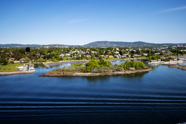 内奥斯陆峡湾，在挪威奥斯陆附近，在一个晴朗的日子里，深蓝色的大海和天空，树木繁茂的山丘和红色屋顶的房子图片下载