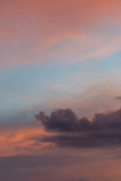 垂直照片，灰色的云衬着蓝色的天空，有些地方是橙色的，被夕阳照亮了。图片下载