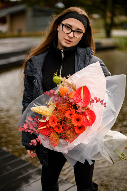 一大束秋天的红色花朵:非洲菊、菊属植物、红掌，一个年轻女子手里拿着一根玉米棒图片下载