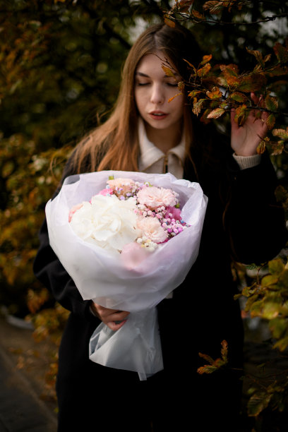 一位漂亮的年轻女子看着一束装在白色包装纸里的粉红色和白色的鲜花图片下载