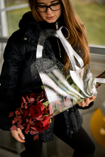 可爱的年轻女子戴着眼镜，拿着一个透明的礼物袋，里面有秋天的红玫瑰图片下载