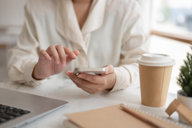 一位女商人坐在咖啡店的桌子上使用智能手机的特写照片。图片下载