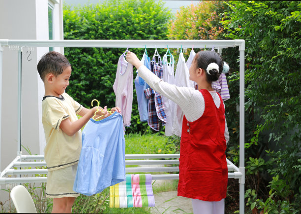 亚洲女孩和男孩在房子附近的花园里帮忙烘干衣服的照片。妹妹和弟弟在帮忙做家务。孩子们把衣服挂在晾衣绳上。图片下载