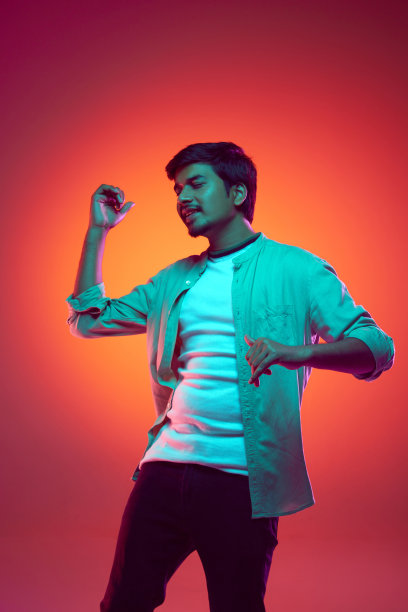 一个穿着休闲服装的阿拉伯青年，在渐变的工作室背景下，在霓虹灯下欢快地跳舞。图片下载