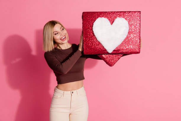 照片可爱漂亮漂亮的女孩穿着时尚的衣服，手拿大红色海报孤立在粉红色的背景图片下载