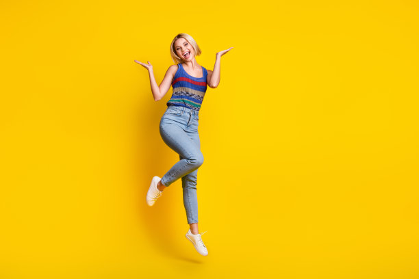 穿着牛仔裤和单衣的活泼有趣的跳跃女人的全身照片，双手向上，在黄色背景上开始孤立图片下载