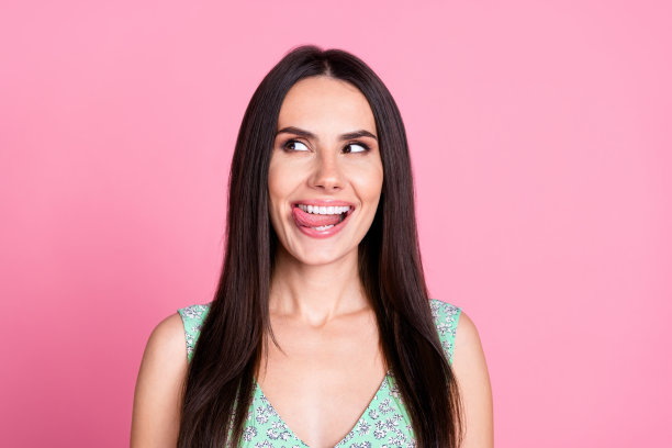 照片中可爱可爱的女人穿着时髦的衣服舔着牙齿，在粉红色的背景下看起来空无一物图片下载