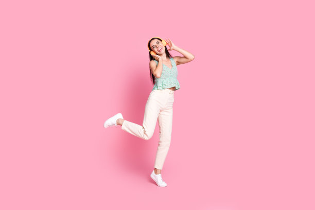 照片中开朗迷人的快乐女子穿着时髦的衣服，在粉红色的背景上享受听音乐图片下载