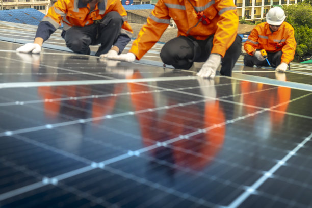 两名工程师检查新安装的黑色太阳能电池板，穿着反光背心的技术人员的倒影模糊。包括带有模糊线路的太阳能电池板的图片。图片下载